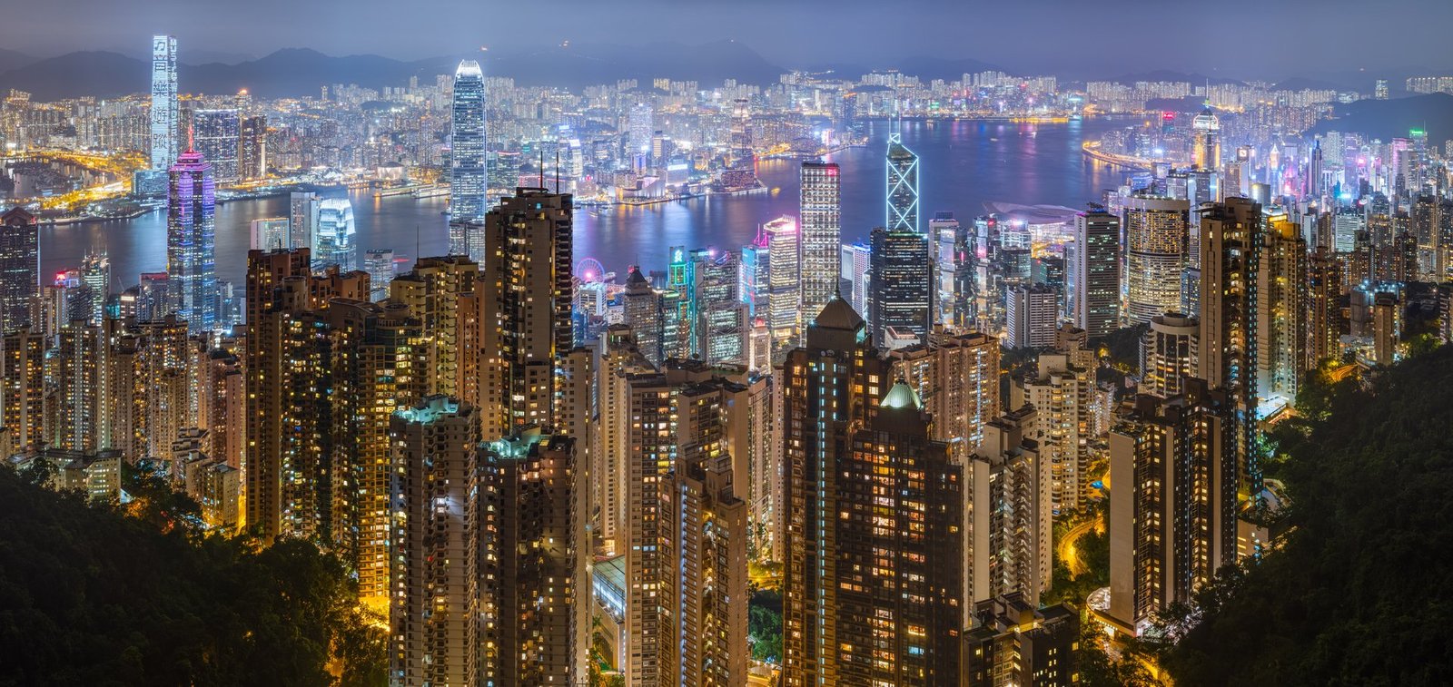 Hong Kong's skyline across Victoria Harbour at night, towers lit in gold and blue
