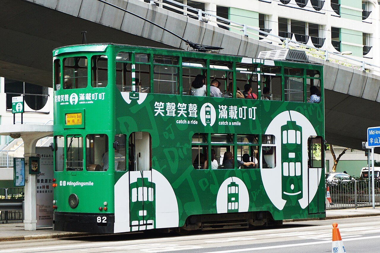 A green Hong Kong double-decker tram in a street between buildings