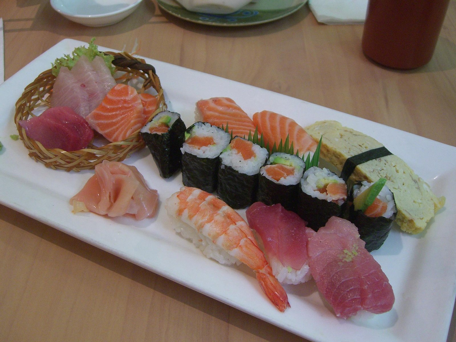 A platter of sushi and sashimi, with nigiri and maki arranged on a white plate