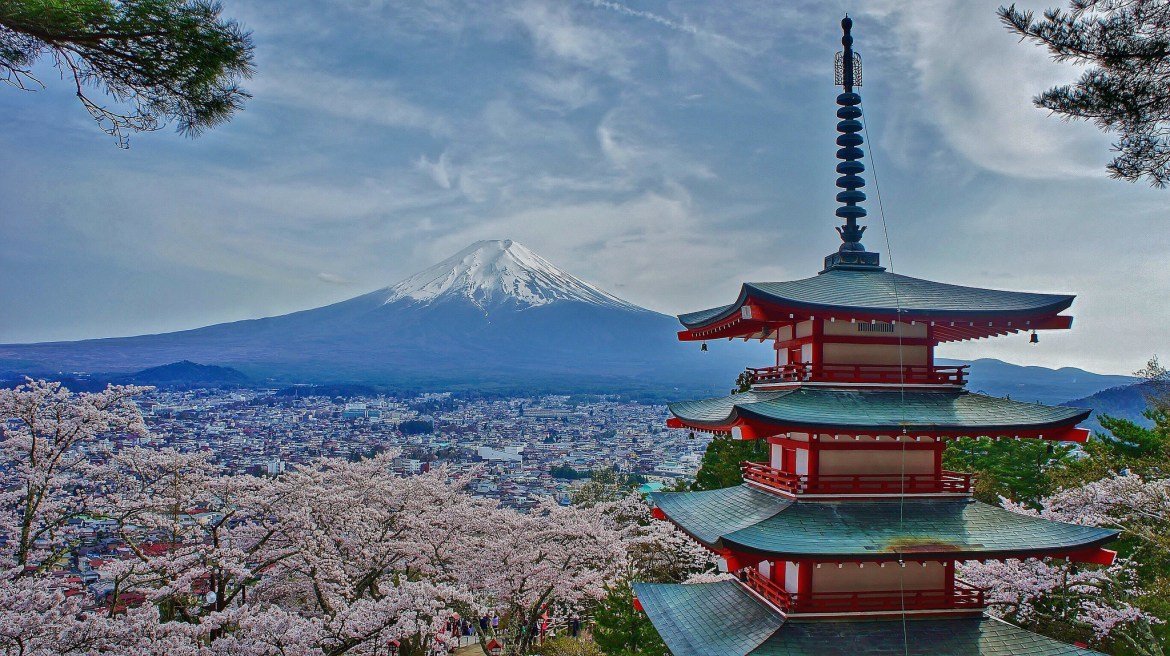 Mount Fuji rising behind the red Chureito Pagoda, framed by cherry blossom