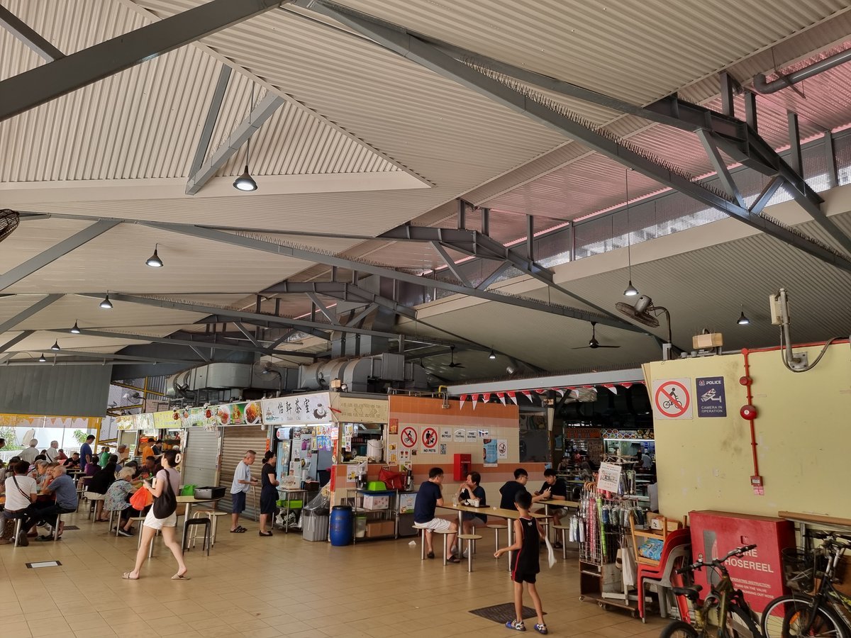 A bustling hawker centre in Singapore, steam rising from food stalls under fluorescent lights